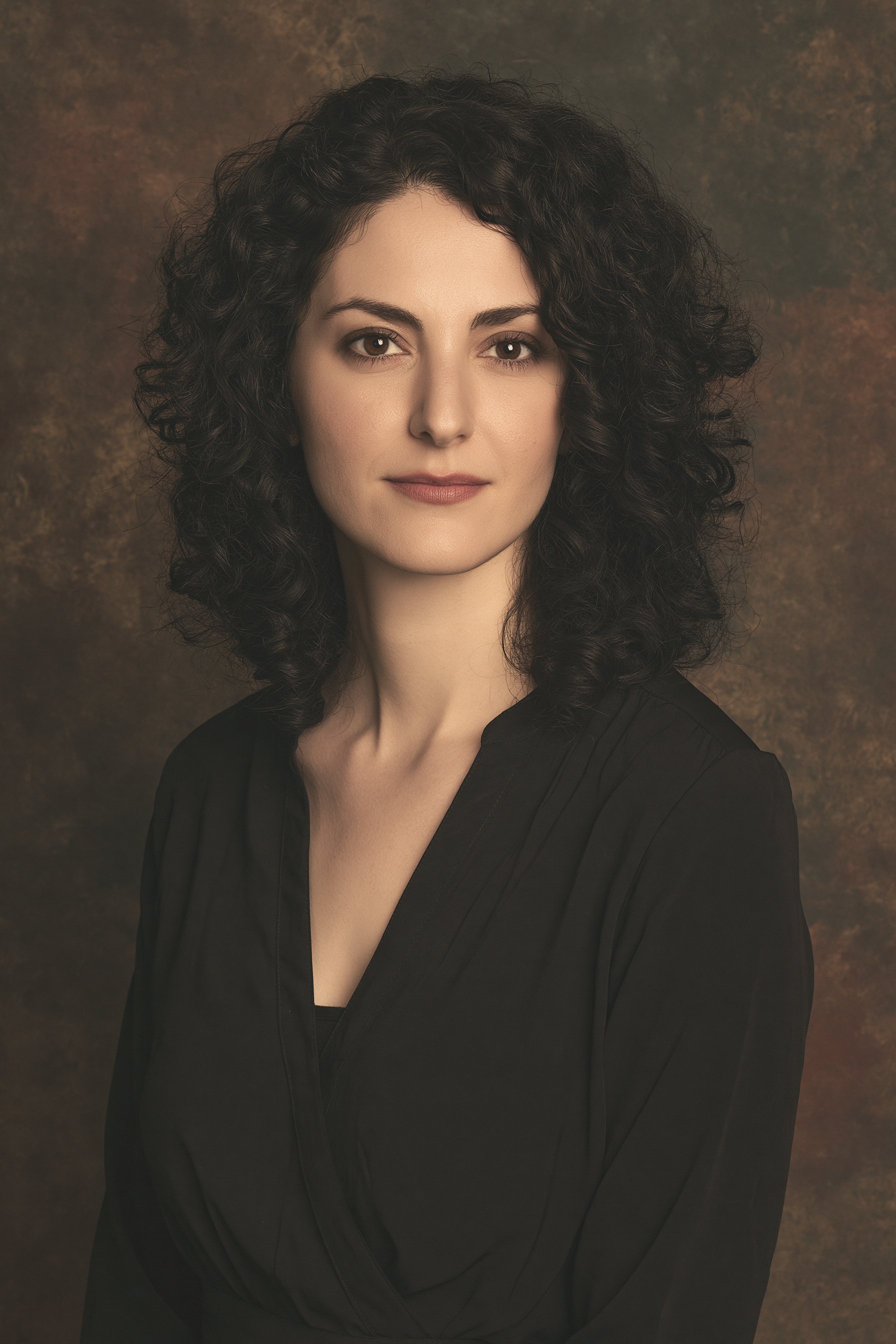 Portrait of Artemis Demetrious, LPC, a counselor with dark curly hair in soft warm light